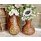 This shows a pair of gourd vases. Each vase is a warm brown and has decorative cats drawn on them. Each vase has a faux flower arrangement. 